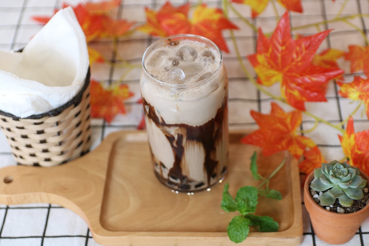 A refreshing iced coffee topped with chocolate syrup, surrounded by autumn leaves and decor.